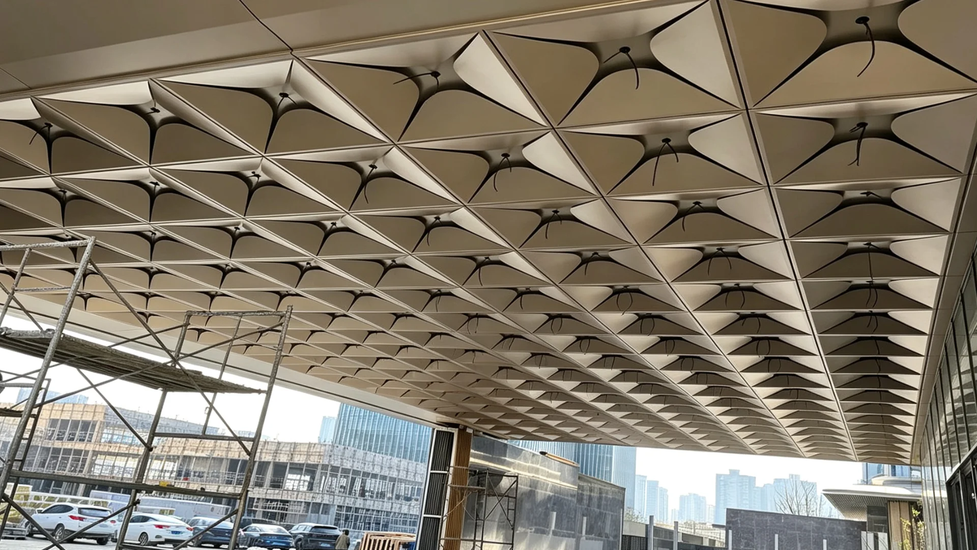 Installation Case of Lindelacr Four-Leaf Petal Aluminum Veneer Outdoor Canopy. Scaffolds, the ceiling of the canopy at the building entrance and continuous petal-shaped aluminum panel modules can be seen at the construction site in daytime. It is applicable to projects including door head canopies, connecting corridors and cornice suspended ceilings.